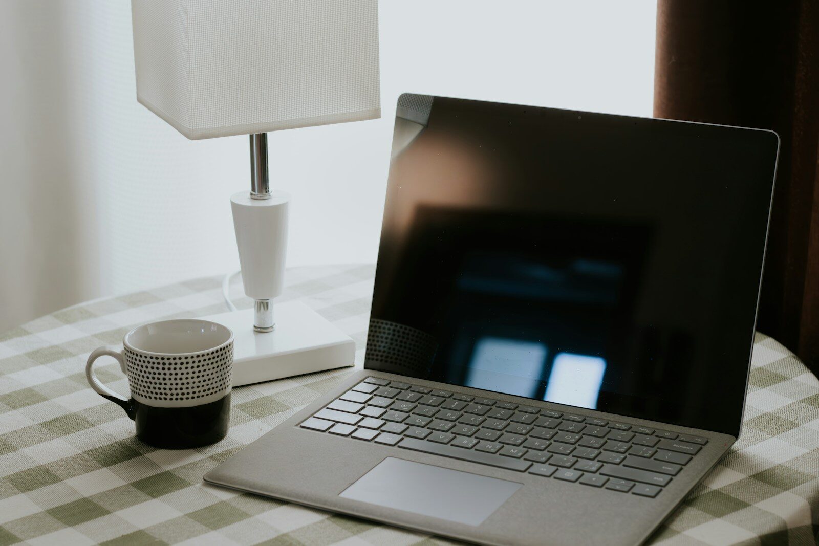 Laptop, mug, and lamp on a checkered tablecloth.